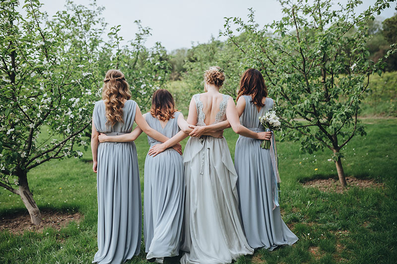 Braut und 3 Brautjungfern stehen mit dem Rücken zum Fotografen, auf einer Wiese.